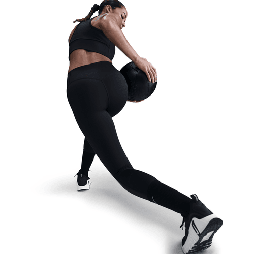 Person in black athletic wear performing a leg exercise with a medicine ball on a white background