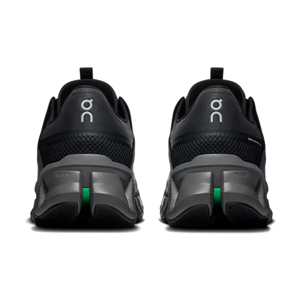 A pair of black and dark gray running shoes shown from the rear, featuring the white 'on' logo on the heel counters and a small green accent on the midsole.