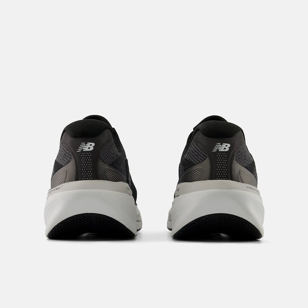 The back of a black running shoes with white soles on a white background