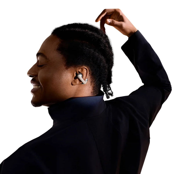 Person wearing a black turtleneck and wireless earbuds, with one hand adjusting hair against a white background