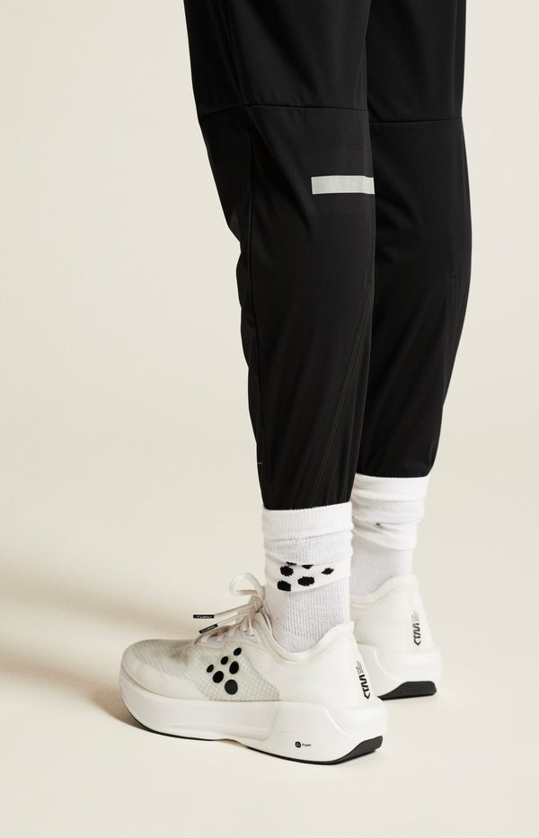 Person wearing black pants, white socks, and white sneakers on a beige background