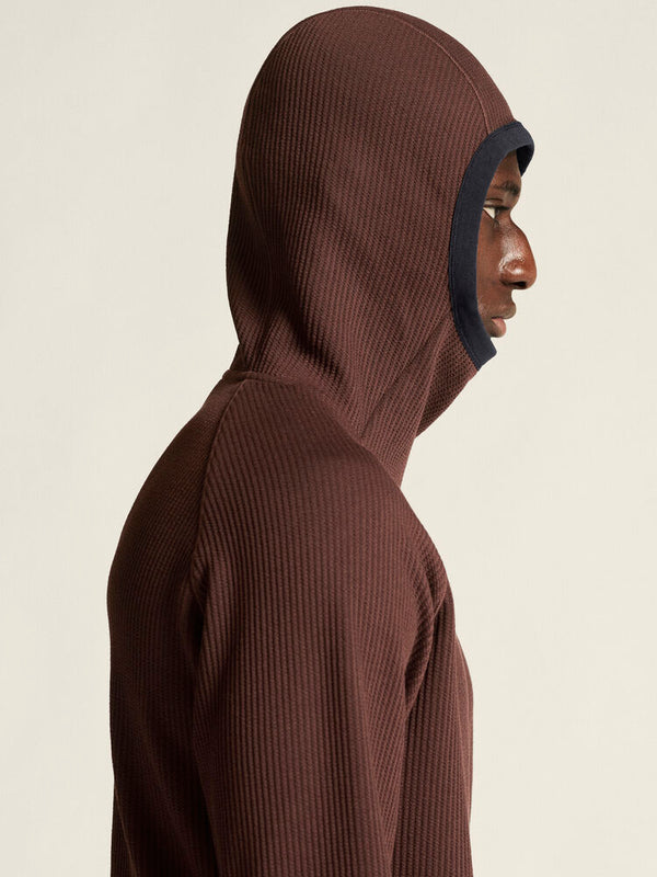 Person wearing a brown hooded garment against a beige background