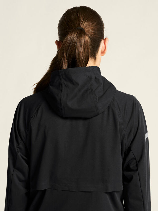 Person wearing a black jacket with a hood on a beige background