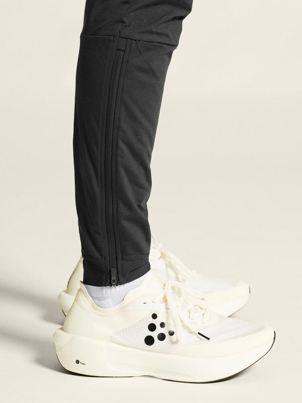 Person wearing black pants and white sneakers on a light background