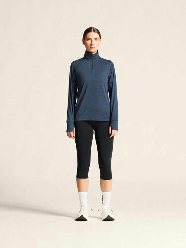 Person wearing a blue long-sleeve top and black leggings on a beige background