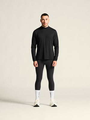 Man wearing a black long-sleeve top and leggings on a beige background