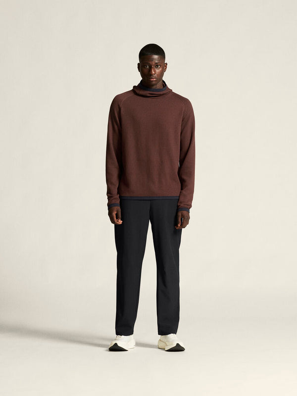 Man wearing a brown sweater and dark pants on a plain background