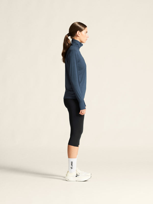 Woman wearing a blue turtleneck and black leggings on a beige background