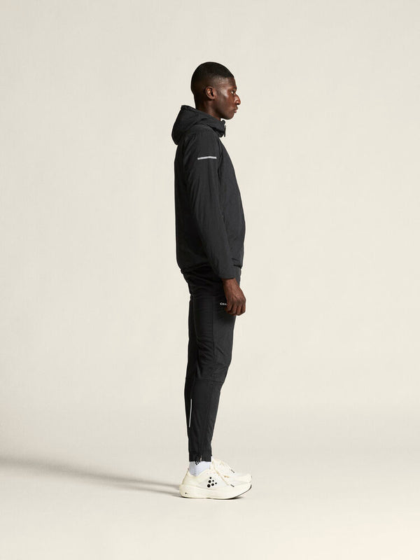Person wearing a black tracksuit with white sneakers on a beige background