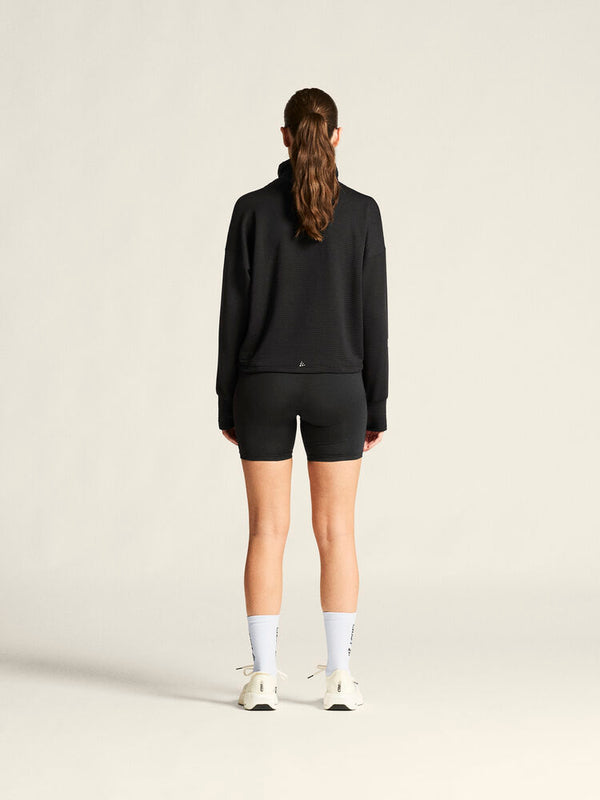 Person wearing a black tracksuit and white sneakers on a plain background