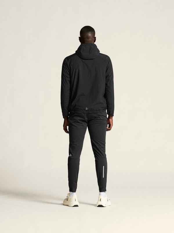 Person wearing a black tracksuit with a hood on a light gray background