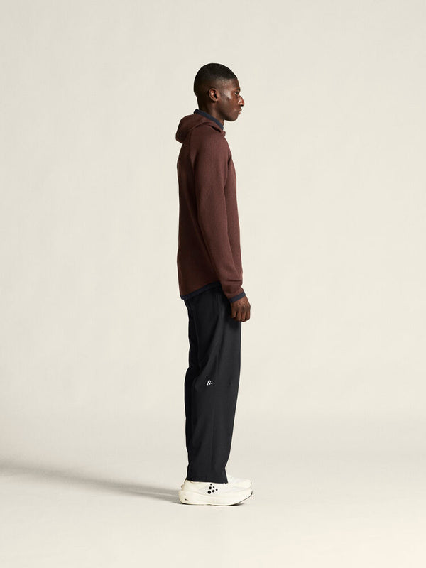 Person wearing a brown hoodie and black pants on a beige background