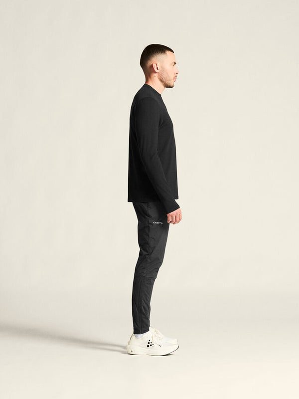 Man wearing a black sweater and dark pants standing against a plain background