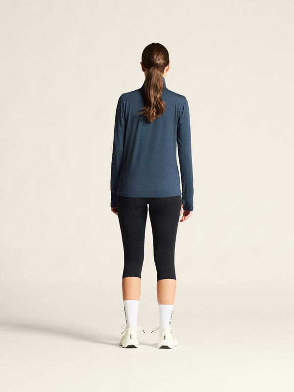Person wearing a blue long-sleeve top and black leggings on a beige background