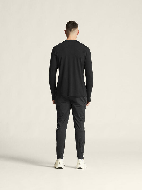 Person wearing a black long-sleeve top and pants on a beige background
