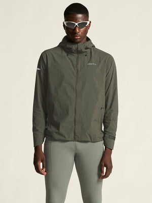 Person wearing a green jacket and pants with sunglasses on a beige background