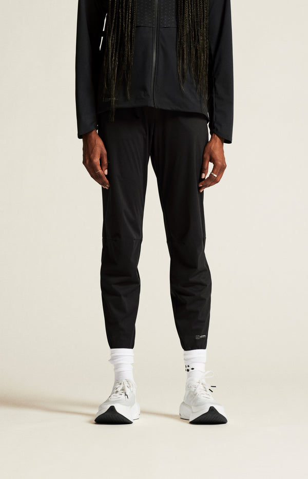 Person wearing black pants and a black jacket on a beige background