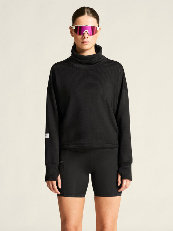 Person wearing a black sweatshirt and shorts with reflective sunglasses on a beige background