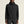 Person wearing a black jacket with a brand logo on a beige background