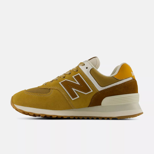 A New Balance 574 sneaker in a mustard yellow and brown colorway, featuring a white outlined 'N' logo on the side, cream midsole, and brown gum outsole, shown in profile against a light gray background.