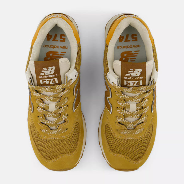 A pair of New Balance 574 sneakers in a mustard yellow and beige colorway, shown from a top-down view on a light gray background.
