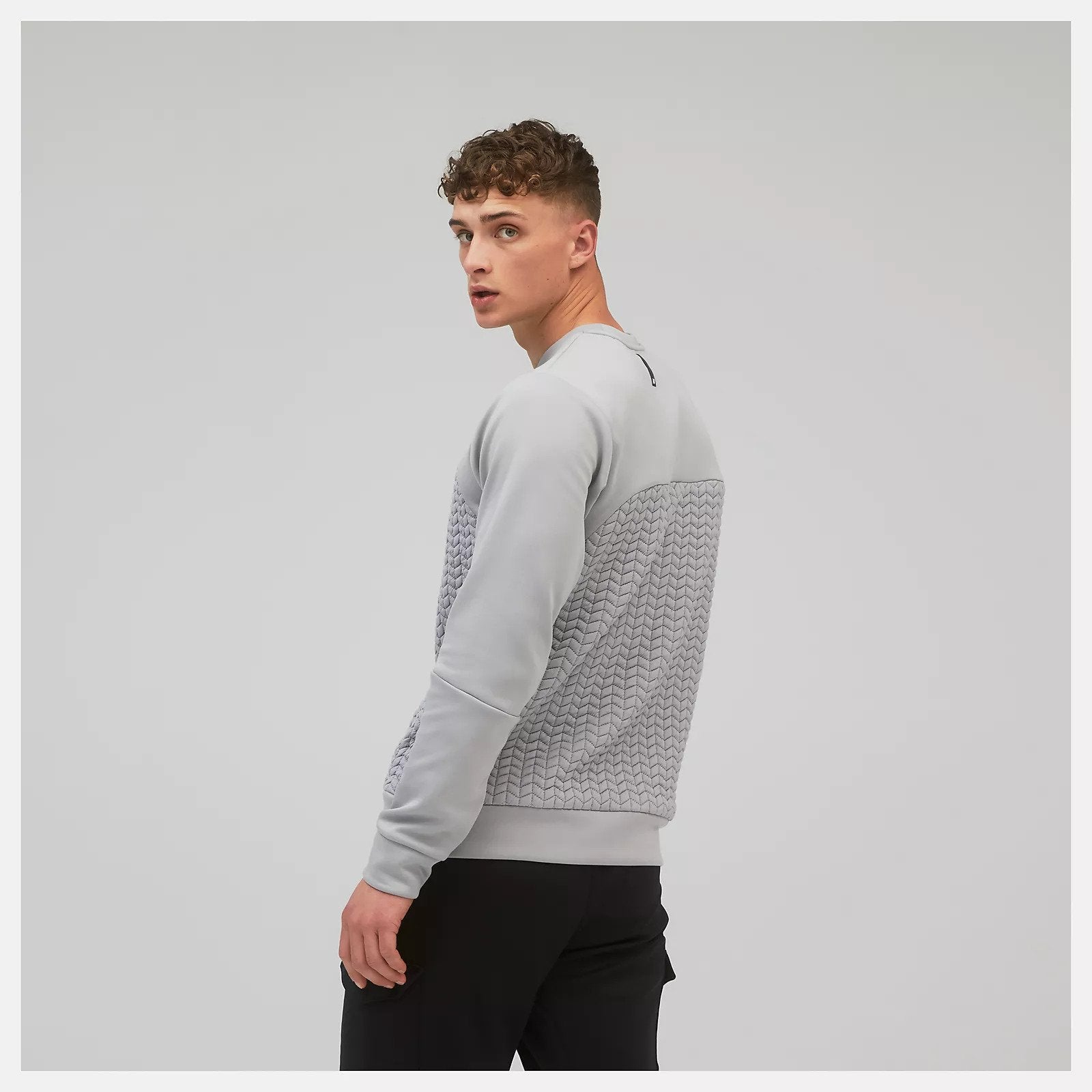 Back angled view of a model wearing the Men's Heatloft Crew by New Balance in the color Alloy