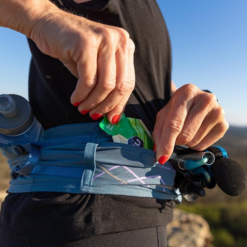 Zoomed in view of a nutrition gel going in one of pouches of the VaporHowe Waistpack from Nathan in the color Blue Mirage/Lupine
