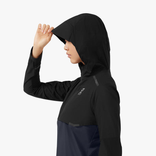 Side view (with the hood up) of a model wearing the Women's Weather Jacket from ON in Black/Navy
